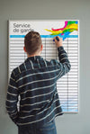 Person writing on a large chart titled 'Service de garde' against a gray wall.