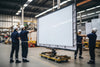 Workers handling a large flat panel screen in a warehouse setting