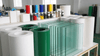 Green glass panels and rolls of paper or film on a stand in a workshop setting.